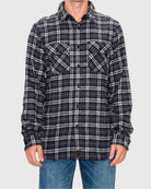 Person wearing a black and white plaid shirt with rolled-up sleeves on a gray background