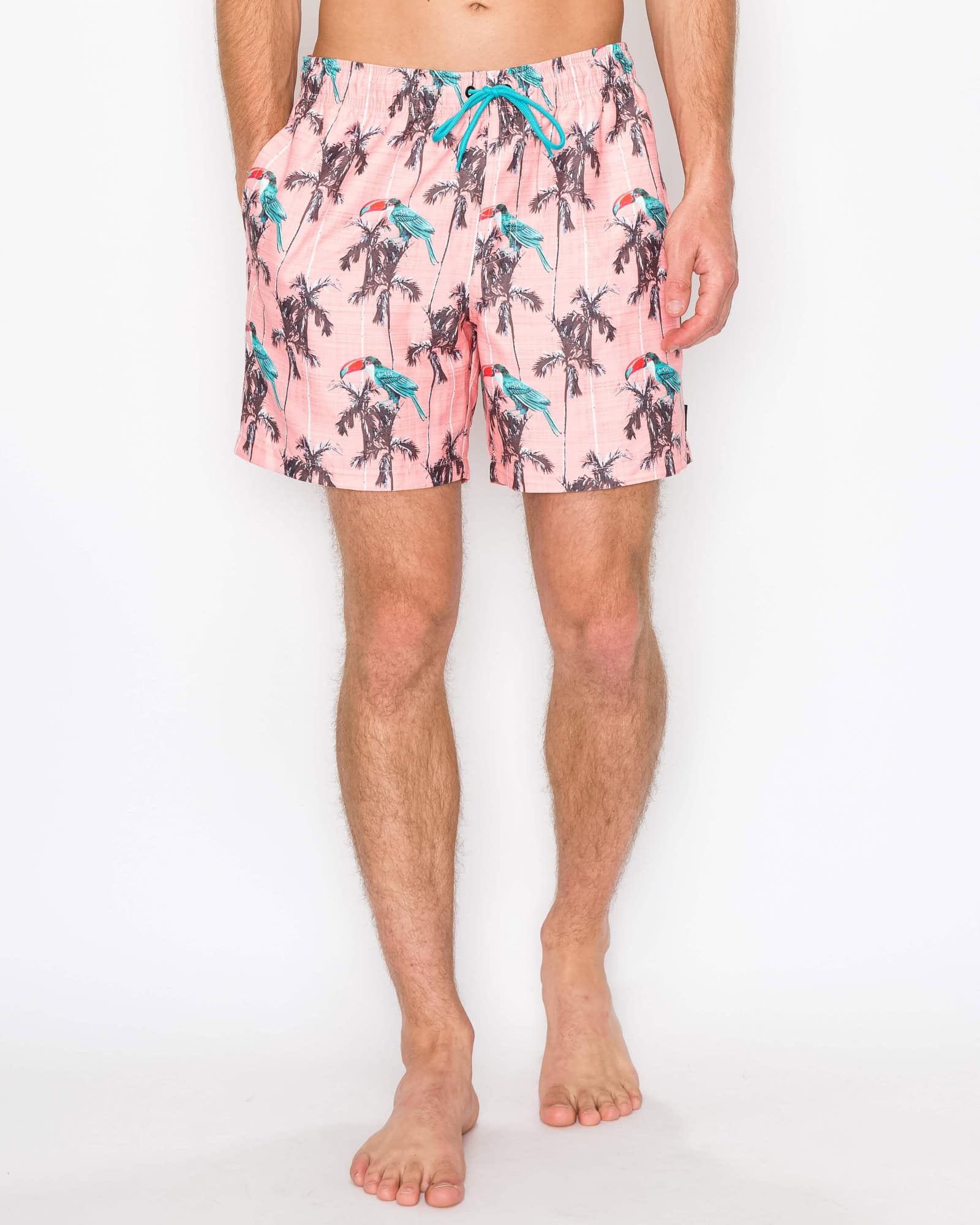 Person wearing pink swim shorts with palm tree and bird pattern on a white background