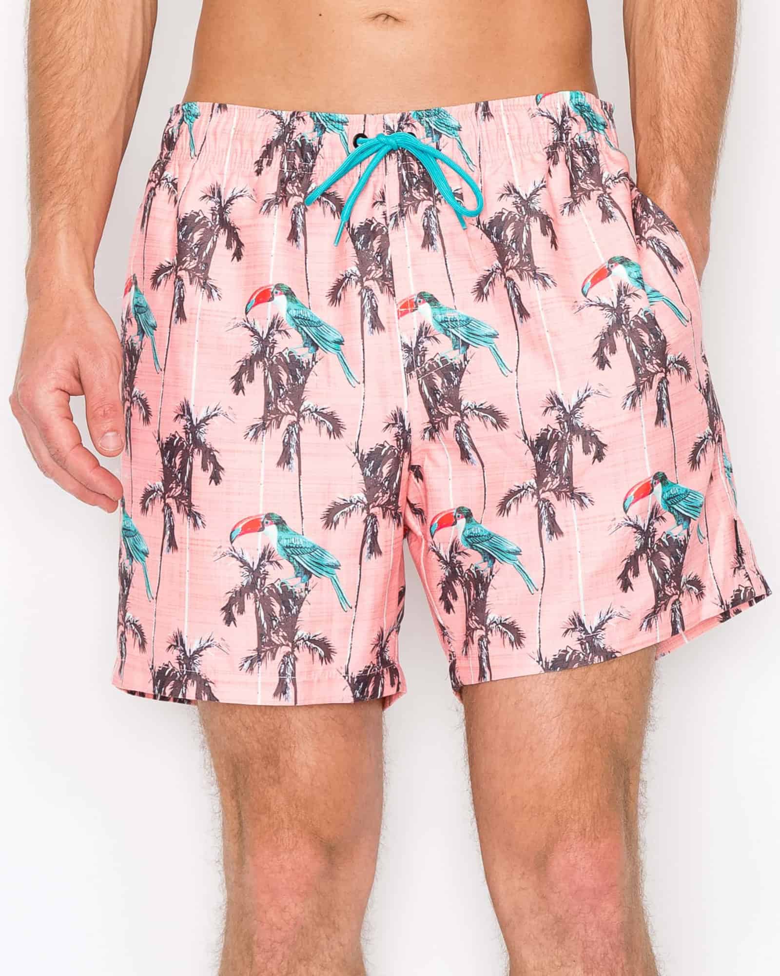Pink swim shorts with parrot and palm tree pattern on a white background