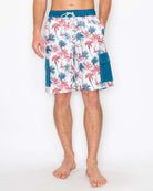 Front view of model wearing men’s boardshorts with red and blue palm tree print, showing below-the-knee length and relaxed fit.