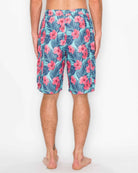 Back view of model wearing Men’s Paradise Bloom Cargo Boardshorts, displaying pink tropical flowers on a blue background, below-the-knee length.