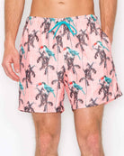 Pink swim shorts with parrot and palm tree pattern on a white background